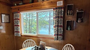 Ein Esszimmer mit Holzboden, einem runden Tisch, weißen Stühlen, einem Fenster mit Vorhängen und einer Deckenleuchte.