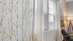 A room with a patterned wallpaper, a window with blinds, a chair, and a lamp. - Luxe Downtown Townhome-Sleeps 6 Brand New Build! (Indianapolis)