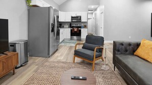 A modern kitchen with stainless steel appliances, a dining area with a grey sofa and a small coffee table, and a TV on the left. - Luxe Downtown Townhome-Sleeps 6 Brand New Build! (Indianapolis)