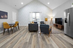 Ein modernes Wohnzimmer mit Essbereich, einer Couch, einem Fernseher und einem Kühlschrank.