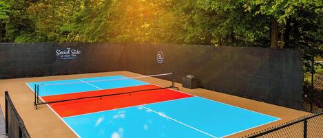 An outdoor tennis court with a net, surrounded by a chain-link fence, and a sign that reads 'The Social Side of Torch Lake.'