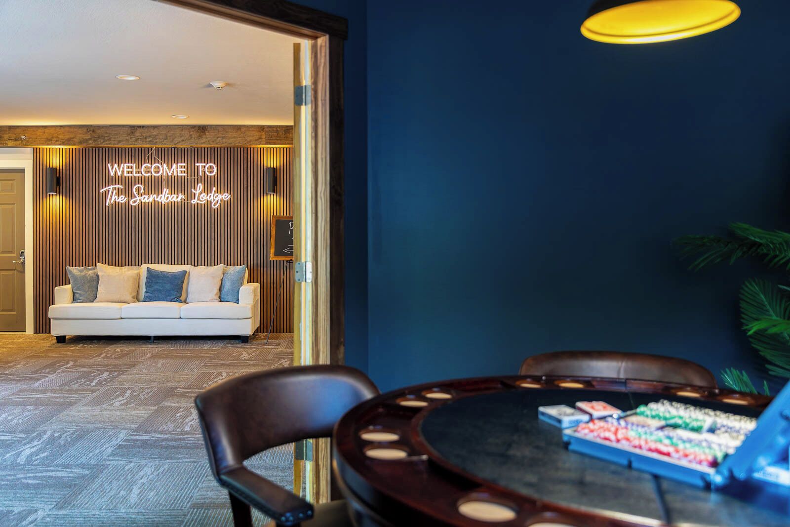 Een modern interieur met een bank en een neonbord waarop 'WELCOME TO The Sandman Lodge' staat.