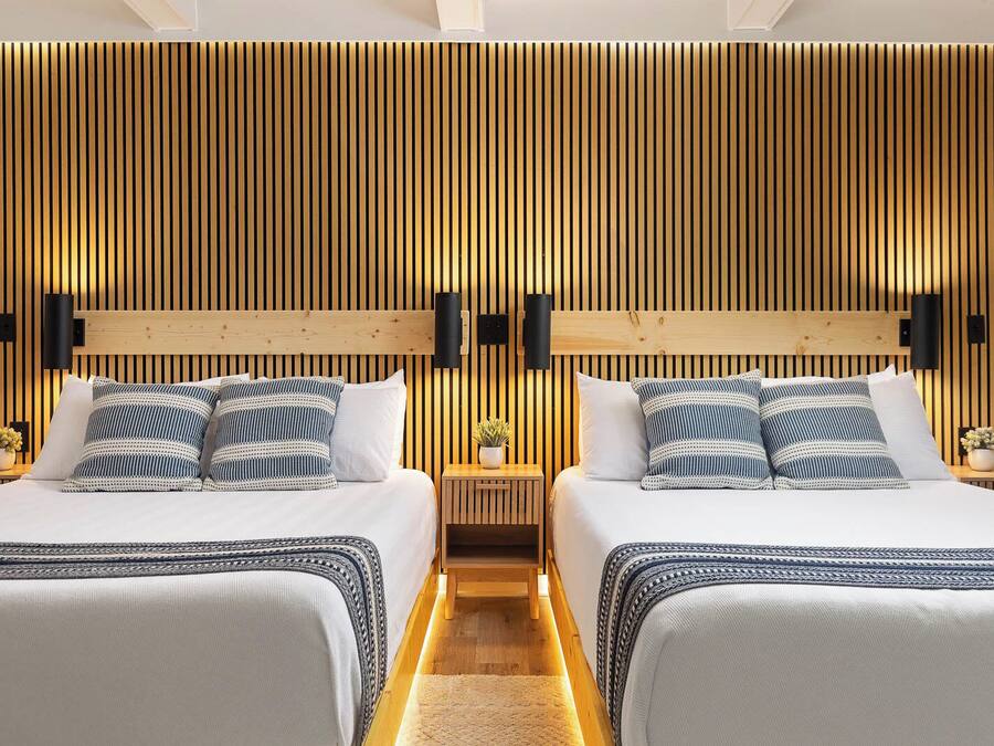 Habitación de hotel con dos camas, paneles de madera en las paredes y lámparas de noche.