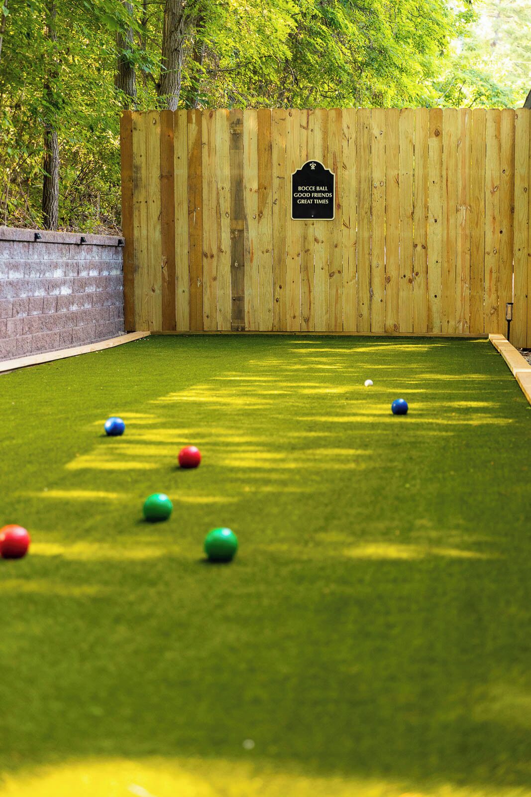 Een jeu de boules baan met een houten omheining, kunstgras en een bord waarop staat: 'BOCCE BALL GOOD FRIENDS GREAT TIMES'.