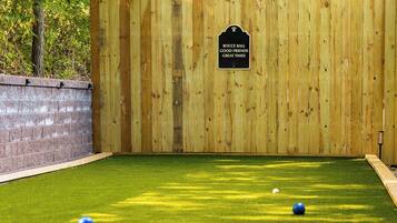 Een jeu de boules baan met een houten omheining, kunstgras en een bord waarop staat: 'BOCCE BALL GOOD FRIENDS GREAT TIMES'.