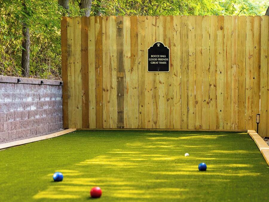 Een jeu de boules baan met een houten omheining, kunstgras en een bord waarop staat: 'BOCCE BALL GOOD FRIENDS GREAT TIMES'.