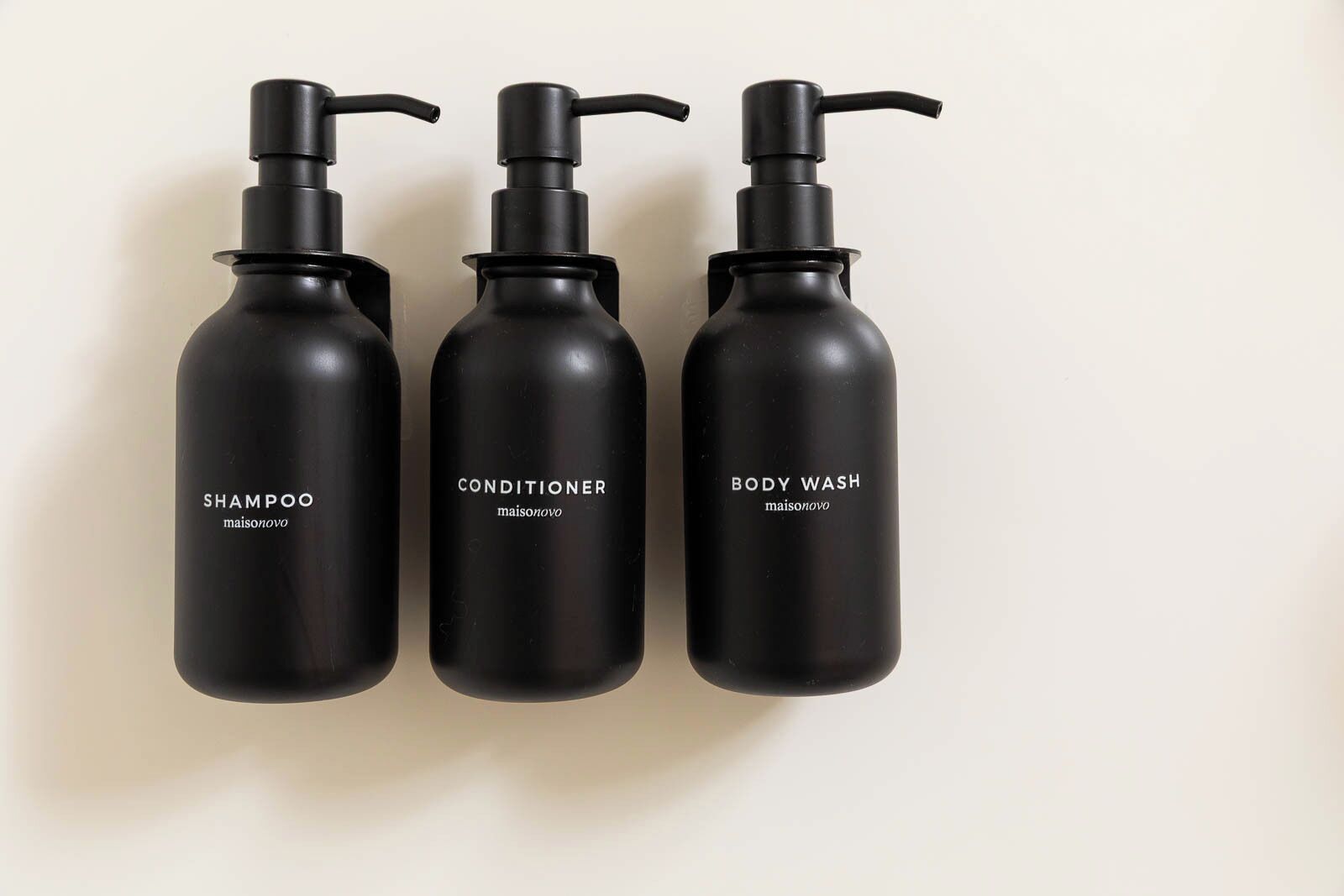 Three black bottles with pumps, labeled 'SHAMPOO,' 'CONDITIONER,' and 'BODY WASH,' all from the brand 'maisonovo.'