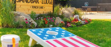 A sign for Sandbar Lodge with Torch Lake written below it, surrounded by a garden with rocks and colorful flowers.