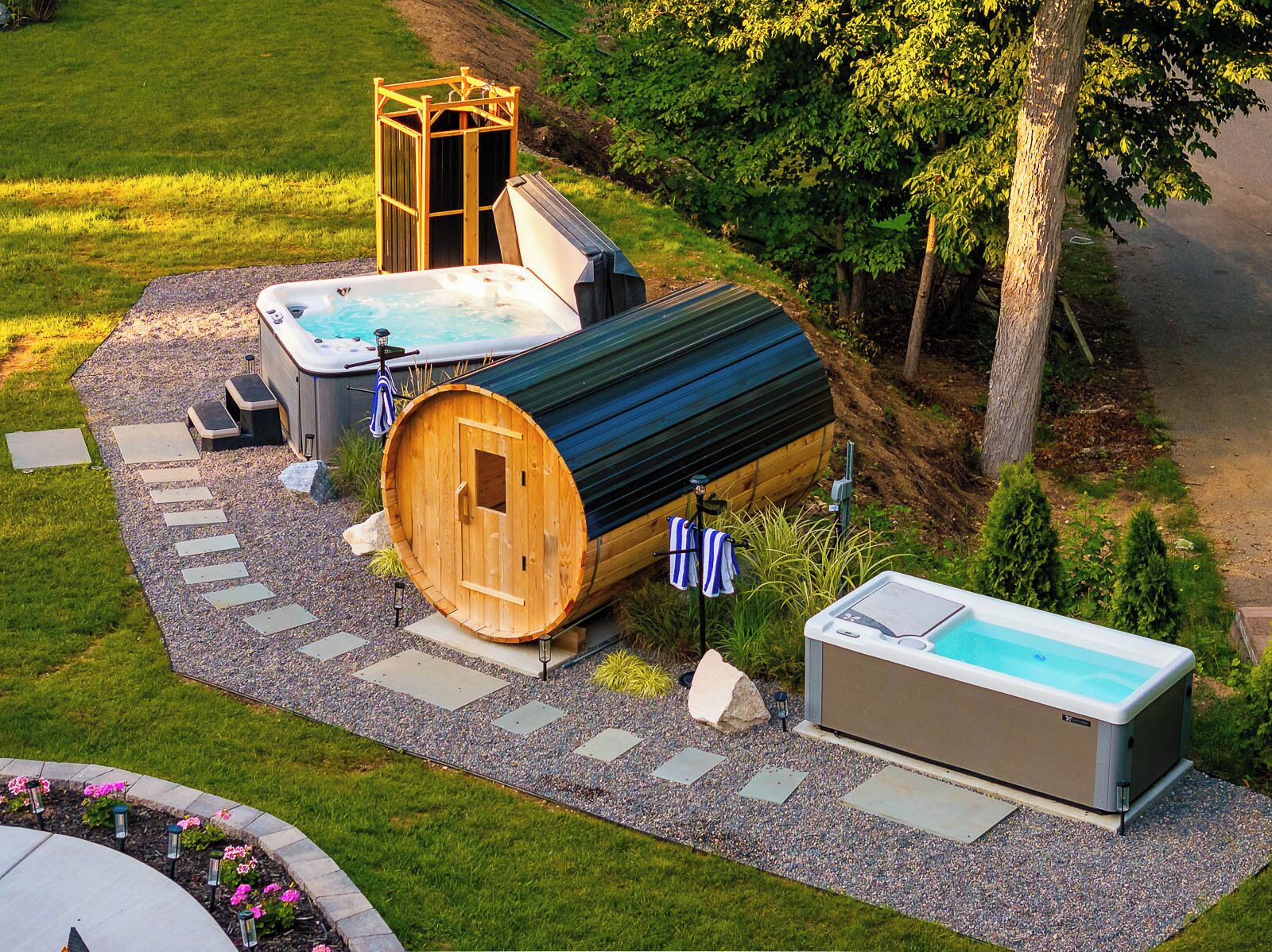 A hot tub and a sauna in a garden setting with a wooden structure and a small pool.