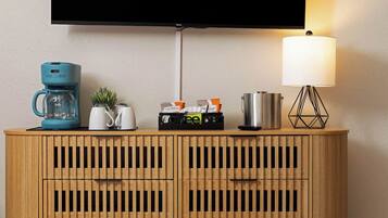 A wooden cabinet with a television mounted above it, a coffee maker, a kettle, a lamp, and a small plant.