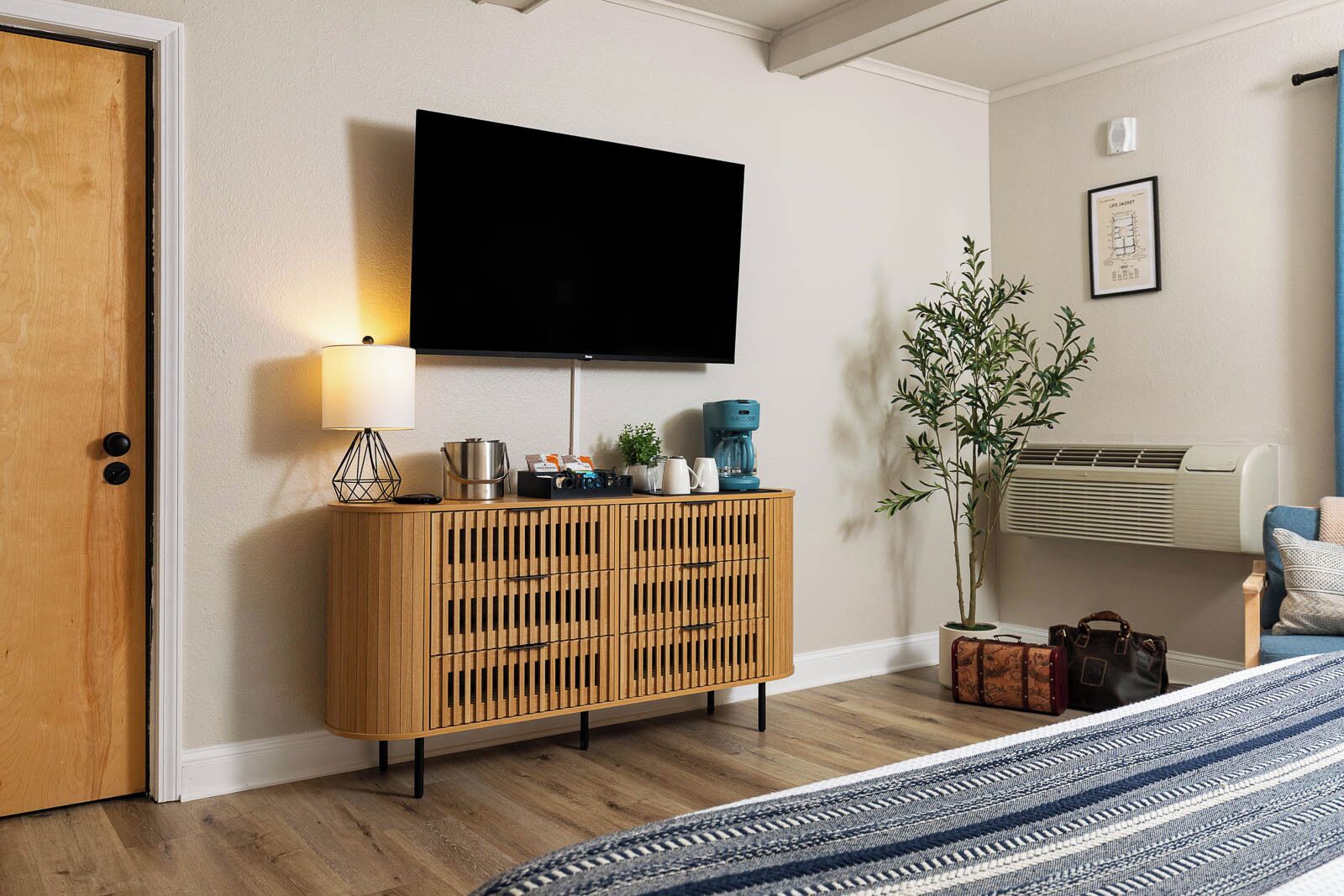 A modern living room with a wooden cabinet, a flat-screen TV, a coffee maker, and a potted plant.