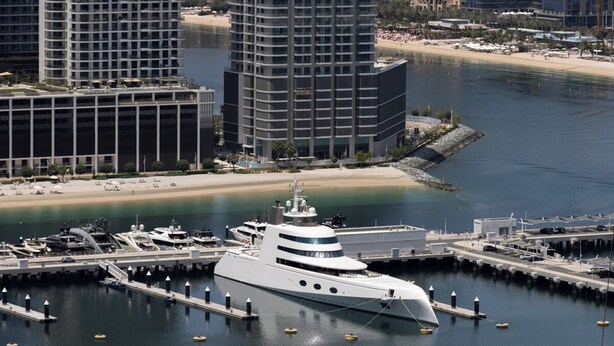 Een jachthaven met een grote jacht afgemeerd, omringd door hoogbouw en een strand.