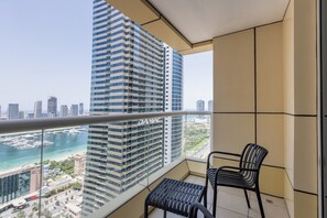 A balcony with a view of a tall building, a chair, and a small table. - Wake Up to Harbour Views | Spacious 2BR | Marina (Dubai)