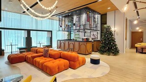 Ein modernes Wohnzimmer mit einer Eckcouch, einem gelben Sessel, einem Weihnachtsbaum und einer Küchenzeile, abgetrennt durch eine Glasscheibe.