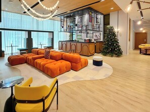 Ein modernes Wohnzimmer mit einer Eckcouch, einem gelben Sessel, einem Weihnachtsbaum und einer Küchenzeile, abgetrennt durch eine Glasscheibe.