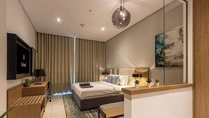 Ein modernes Schlafzimmer mit Bett, Nachttischen, Schreibtisch, Sessel, Fernseher und einem großen Fenster mit Vorhängen.