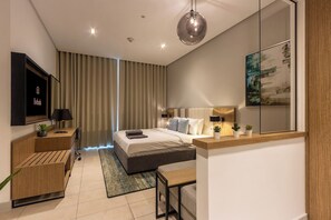 Ein modernes Schlafzimmer mit Bett, Nachttischen, Schreibtisch, Sessel, Fernseher und einem großen Fenster mit Vorhängen.