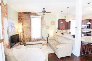 Un salon avec un mur en briques, un canapé, un téléviseur et un ventilateur de plafond.