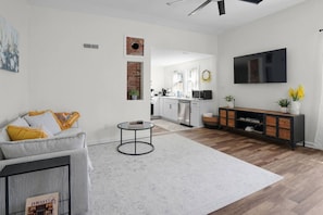 Een moderne woonkamer met een bank, salontafel en een aan de muur bevestigde televisie.