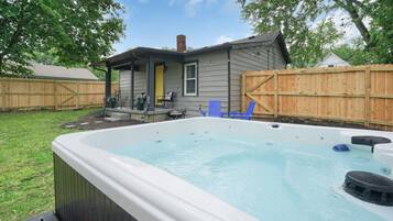 Un patio trasero con un jacuzzi, una terraza de madera y una casa con porche.