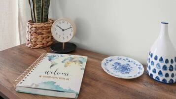 Una mesa de madera con un folleto de bienvenida, un reloj, un florero y un plato.