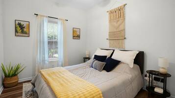 Un dormitorio con cama, mesitas de noche, ventilador de techo, ventana con cortinas y decoración en la pared.