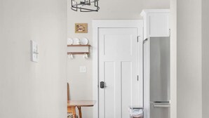 A hallway with a wooden floor, a white door, a dining table with chairs, a hanging light fixture, and a refrigerator. - Chic Downtown Franklin Condo-Sleeps 6! (Franklin)