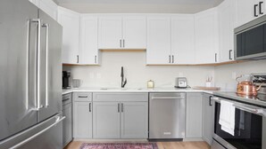 A modern kitchen with white cabinets, stainless steel appliances, and a wooden floor. - Chic Downtown Franklin Condo-Sleeps 6! (Franklin)