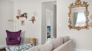 A living room with a purple armchair, a beige sofa, a gold-framed mirror, and a wall-mounted shelf with decorative items. - Chic Downtown Franklin Condo-Sleeps 6! (Franklin)