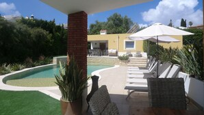 A poolside area with a brick pillar, lounge chairs, and a pergola with an umbrella. - Beautiful villa near Meia Praia, Lagos with solar heated pool & lots of space (Lagos)