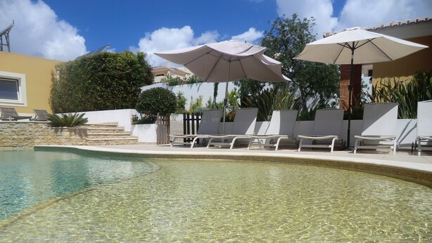 A clear pool with lounge chairs and umbrellas, surrounded by a white wall and greenery. - Beautiful villa near Meia Praia, Lagos with solar heated pool & lots of space (Lagos)