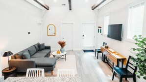 Een ruime woonkamer met een grijze bank, een ronde salontafel en een houten eettafel met stoelen.
