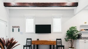 Een eetgedeelte met een houten tafel, twee stoelen, een aan de muur bevestigde televisie en een plant in een pot.