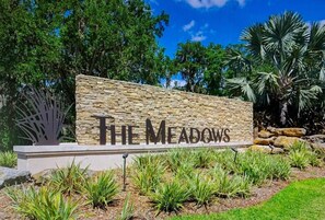 A stone sign with 'The Meadows' written on it, surrounded by landscaped greenery and trees. - Spacious 3-bedroom condo with a golf course view (Sarasota)