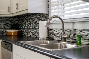 Eine Küche mit einem doppelten Edelstahl-Spülbecken, einem modernen Wasserhahn, einer gefliesten Spritzschutzwand und einem Geschirrspüler.
