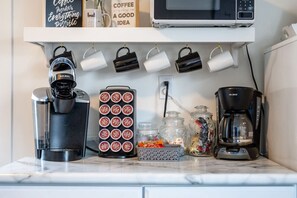 Eine Küchenarbeitsfläche mit Kaffeemaschine, einem Keurig-System, einem Behälter für Kaffeekapseln, Gläsern und einer Mikrowelle.