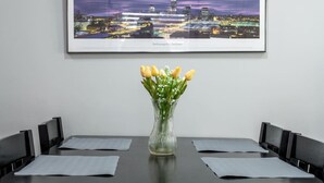 Ett inramat fotografi av en stadsbild, en vas med gula tulpaner och ett bord med stolar.