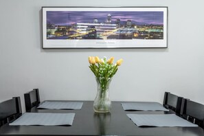 Ein gerahmtes Stadtbild, eine Vase mit gelben Tulpen und ein Tisch mit Stühlen.