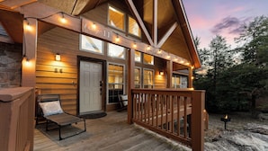 Une cabane en bois avec une véranda, un banc et un foyer extérieur où brûle un feu.