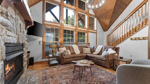 Un salon spacieux doté d’une cheminée en pierre, de grandes fenêtres, d’un escalier en bois et d’un coin salon confortable.