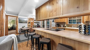 Une cuisine moderne avec des meubles en bois, un îlot central doté de tabourets et une vue sur l’espace repas.