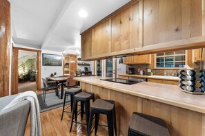 Une cuisine moderne avec des meubles en bois, un îlot central doté de tabourets et une vue sur l’espace repas.