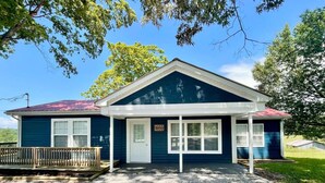 A single-story house with a dark blue exterior, a red roof, and a front porch. - Wolf River Getaway-close to dock (Highway)