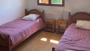 Un dormitorio con dos camas de madera, una mesita de noche y una ventana con la puerta abierta.