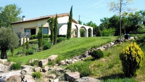 Una casa con fachada blanca, tejado de tejas y jardín con rocas y follaje.