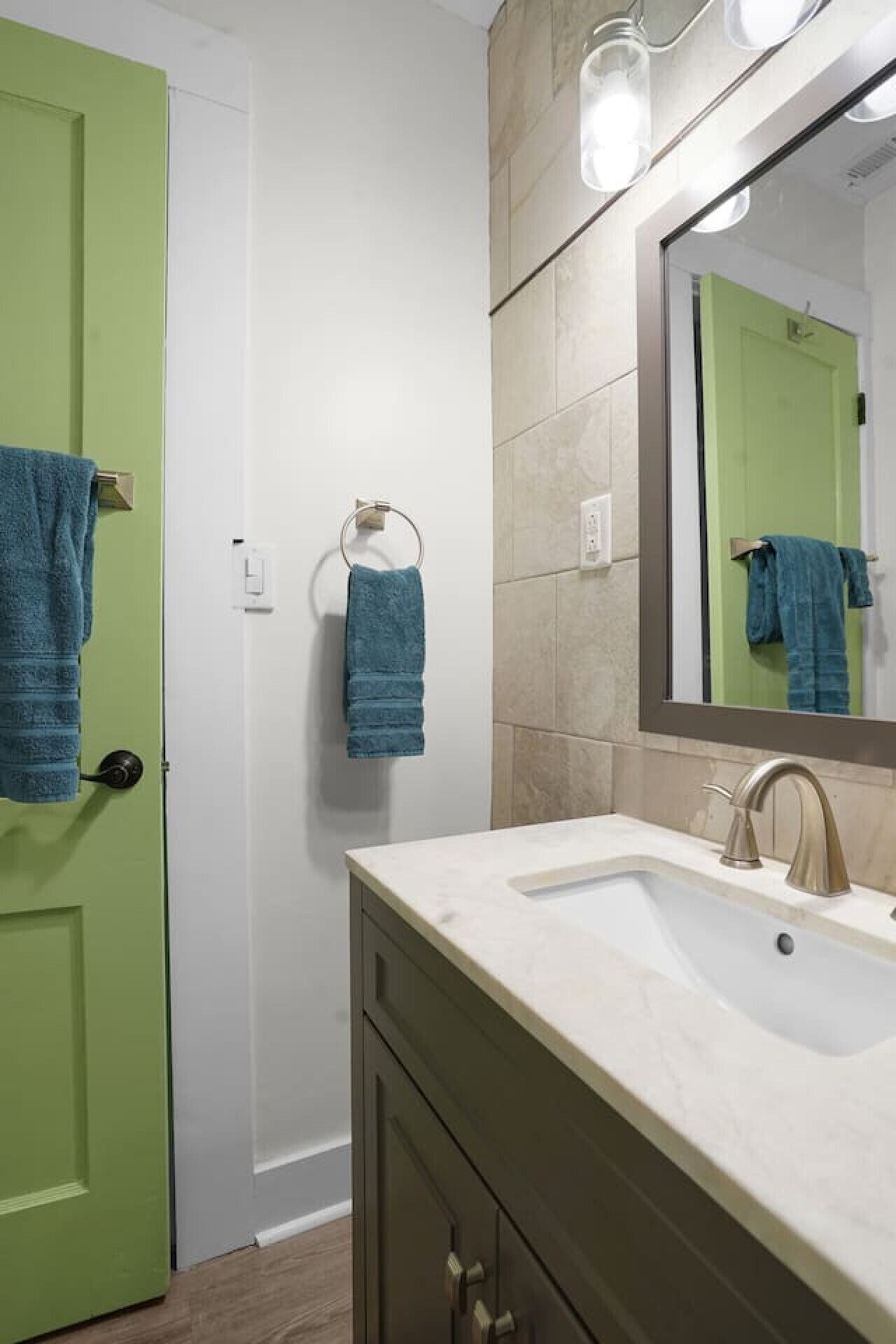 A bathroom with a green door, a sink with a mirror, and two towels hanging on hooks.