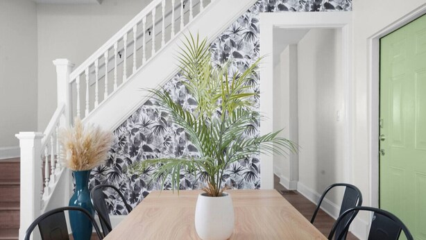 Een eethoek met een houten tafel, stoelen, een potplant, een blauwe vaas en een trap met een witte leuning.