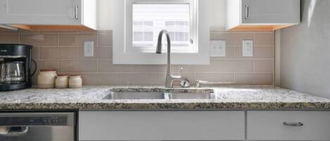 A kitchen with a stainless steel dishwasher, a coffee maker, and a window above the sink.