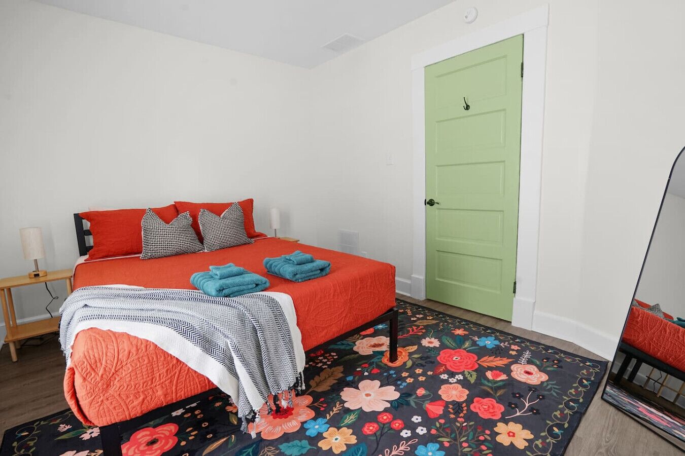 A bedroom with a bed, a nightstand, a green door, and a floral rug.