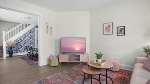 Een woonkamer met een televisie, een bank, een salontafel, een gekleurd vloerkleed en een trap.